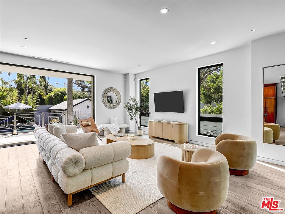 The living room with the western glass wall fully retracted, opening directly onto the pool deck and tropical hillside beyond.