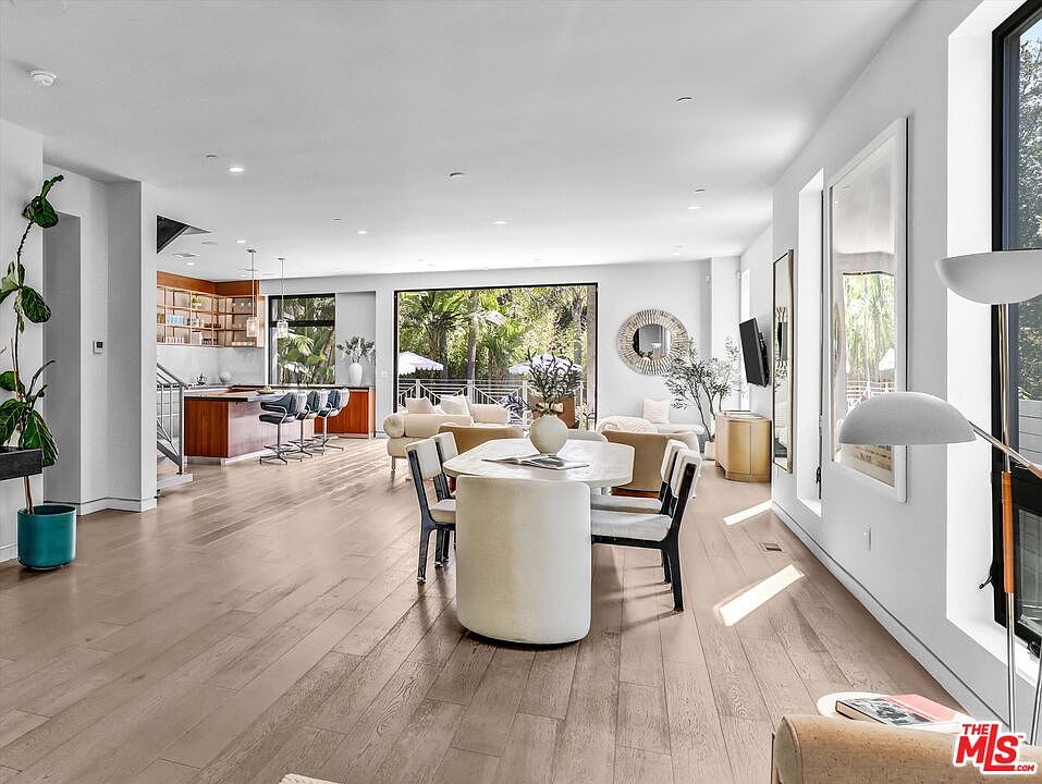Dining table and kitchen island under floating wood cabinetry, with sliding doors framing the pool umbrella outside.