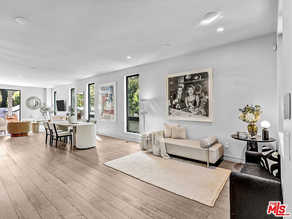 The great room from the entry, with a chaise, vintage gallery art, and dining beyond, anchored in wide-plank wood.