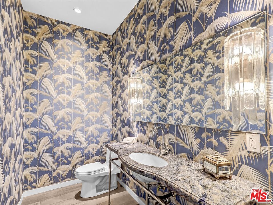 The powder room, with deep blue palm-frond wallpaper, a marble vanity, and a tall slim sconce.